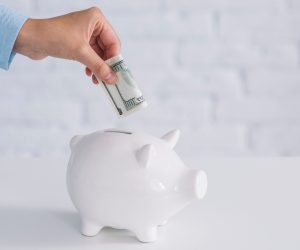 mano-humana-insertando-billetes-en-piggybank-blanco-en-el-escritorio